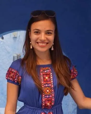 Anca Florea al aire libre, sonriendo delante de un muro de piedra